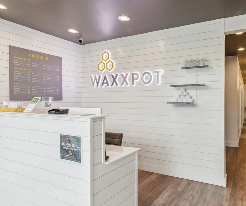a white reception desk with a white counter top and a neon sign that says wax