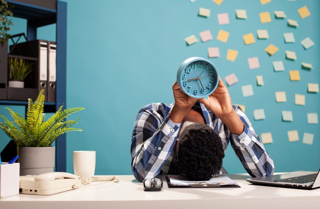 a man sitting at a desk with a clock over his head