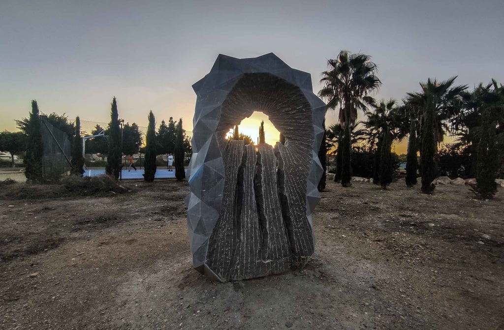Modern geometric stone sculpture in an outdoor park at sunset with palm trees.