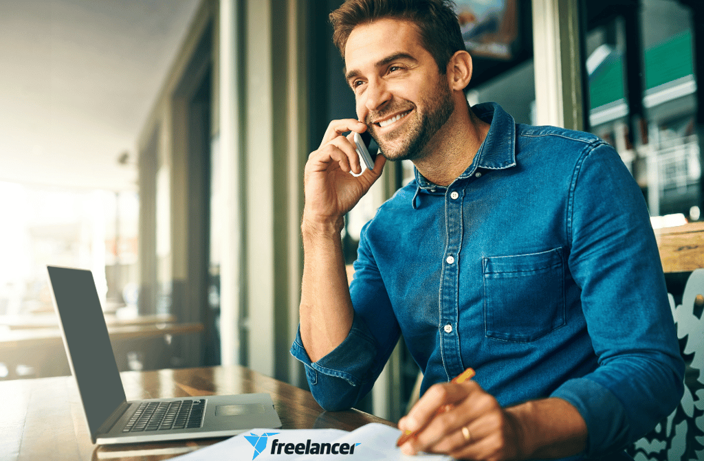 a man sitting at a table with a laptop and a notebook and making a phone call