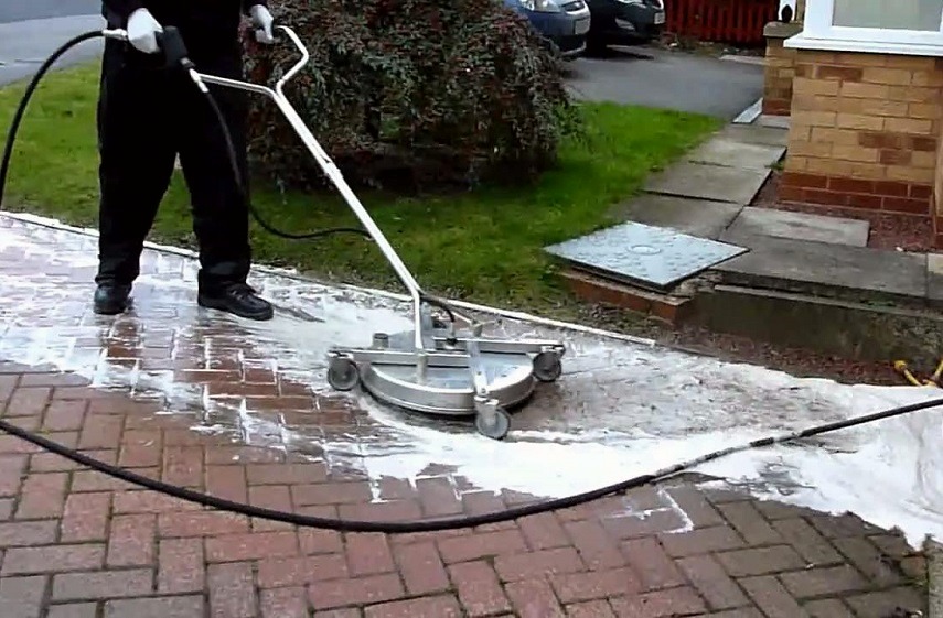 A man using a surface cleaner to clean a brick paver path