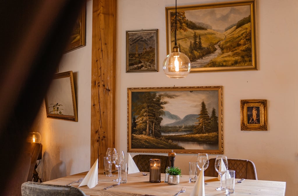 Elegant gedeckte Restauranttische mit edlem Glasgeschirr und Landschaftsgemälden an der Wand.