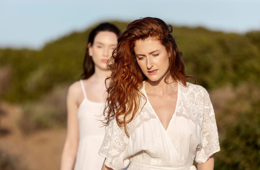 two unhappy women in white dresses standing in a field