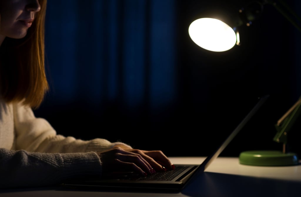 a woman is sitting at night at a desk with a laptop