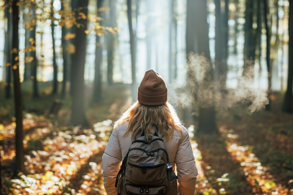A woman in a hat and backpacker walking through a forest