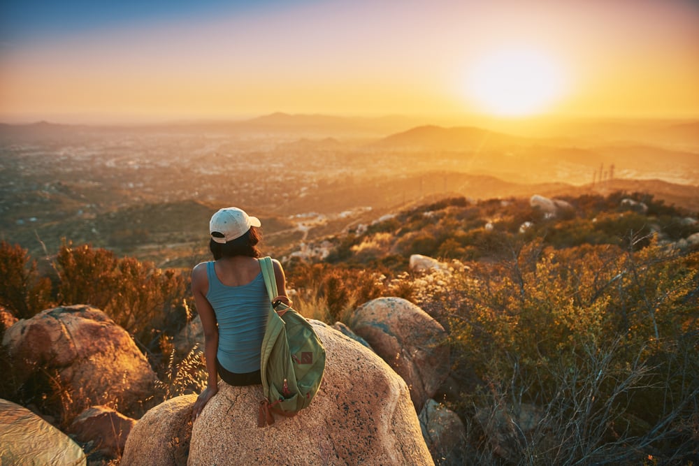 A woman sitting on a rock looking at sunset at peace