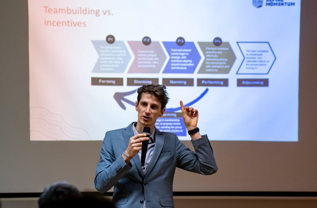 A male speaker presenting Tuckman's stages of team development at a corporate teambuilding workshop.