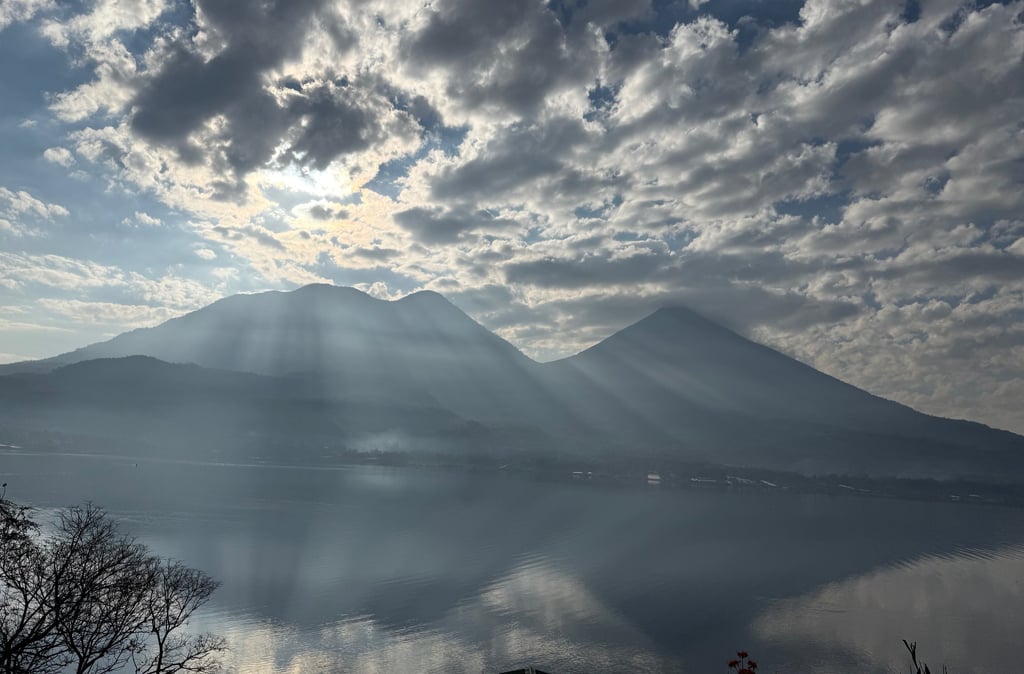 Sunlight rays piercing through clouds over a volcanic mountain lake landscape at dawn.