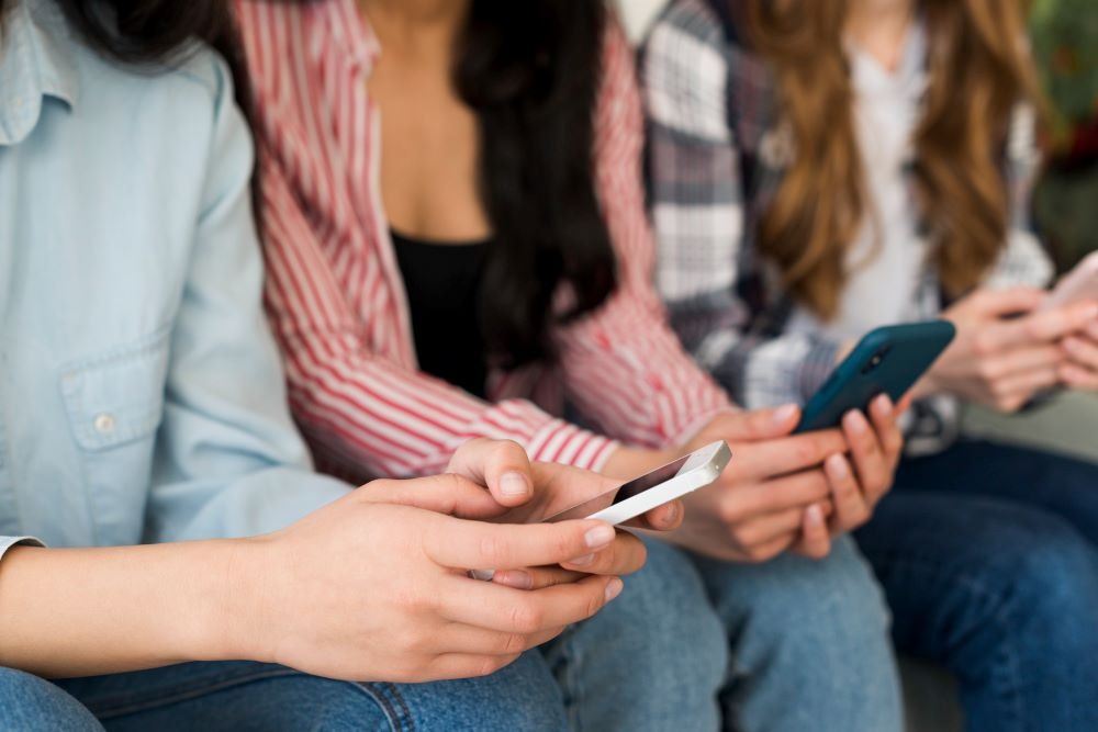 a group of people sitting on a bench with cell phones