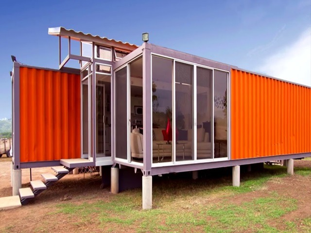 Modern orange shipping container home featuring glass walls and a raised foundation.