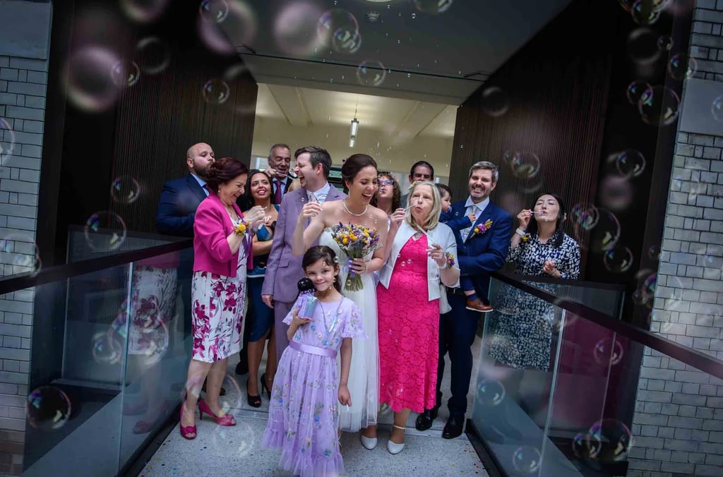 A joyful wedding couple and their guests are showered with bubbles in Lambeth Town Hall