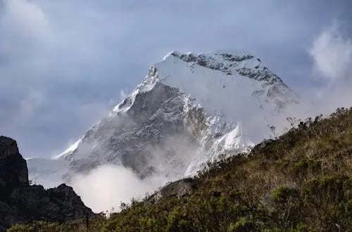 Image of Mount Kilimanjaro’s snow-capped peak surrounded by clouds, with green foothills in the fore