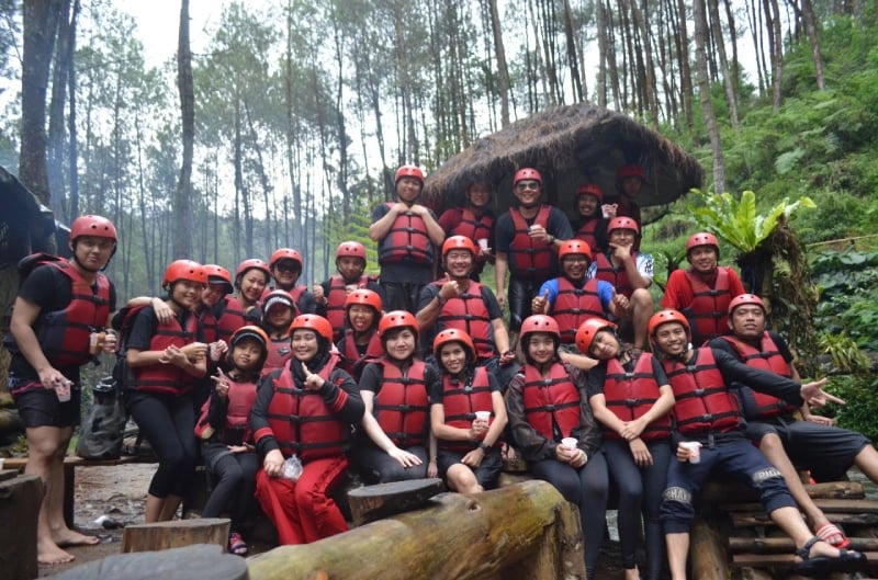 Foto karyawan perusahaan saat gathering atau team building outdoor, mengenakan alat keselamatan arung jeram di tengah hutan p