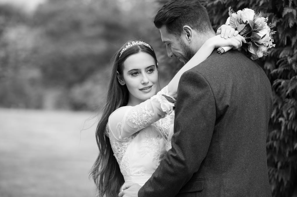black and white photo of bride and groom, bride looking into distance, groom looking at bride and smiling, blurry background