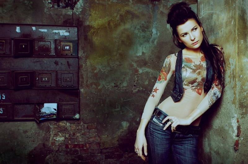Audrius Turskas photography a woman with tattoos on her chest standing next to old textured wall