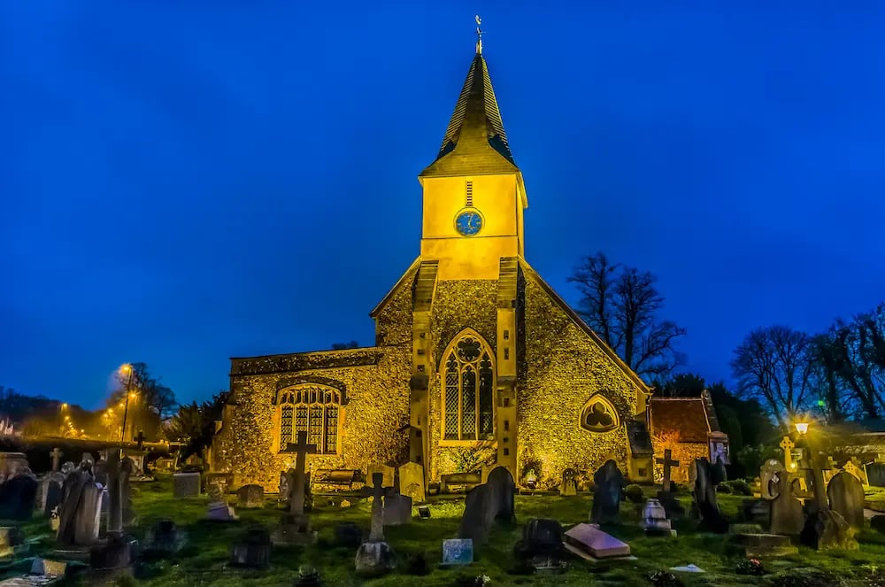 Illuminated historic stone church with a clock tower and cemetery in Sanderstead