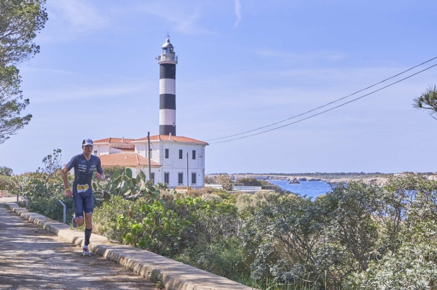 a man running on a path with a lighthouse in portocolom