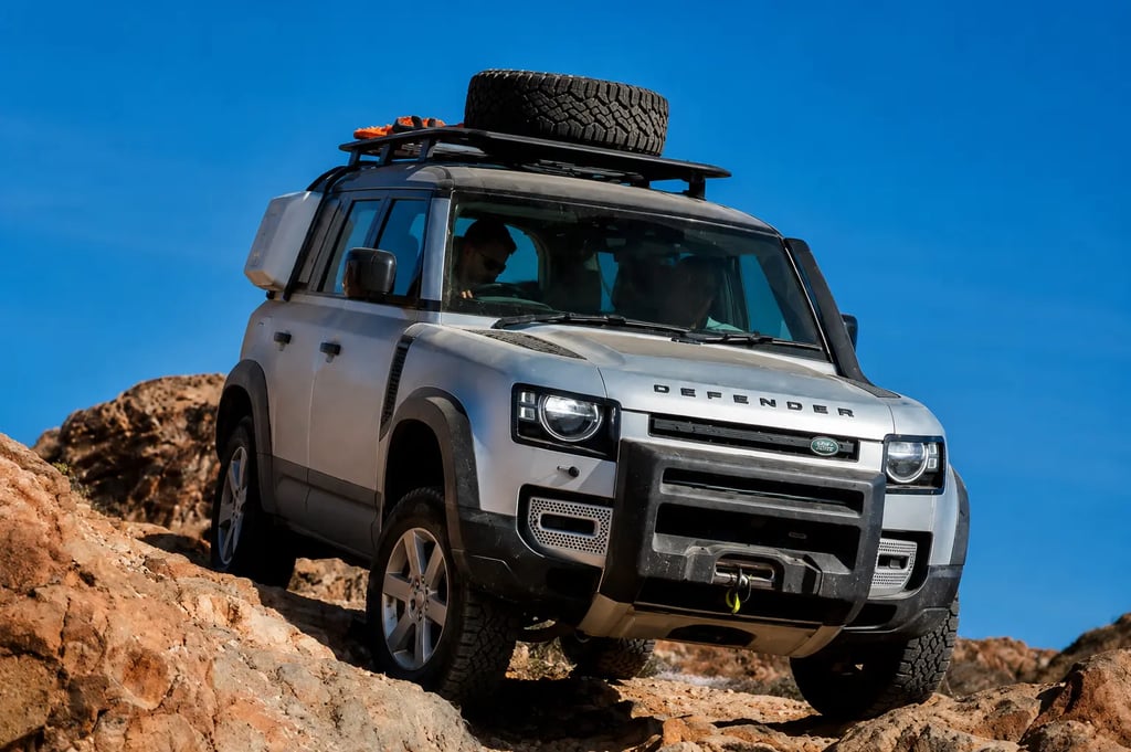 Land Rover Defender prata enfrentando trilha rochosa em cenário off-road com céu azul ao fundo