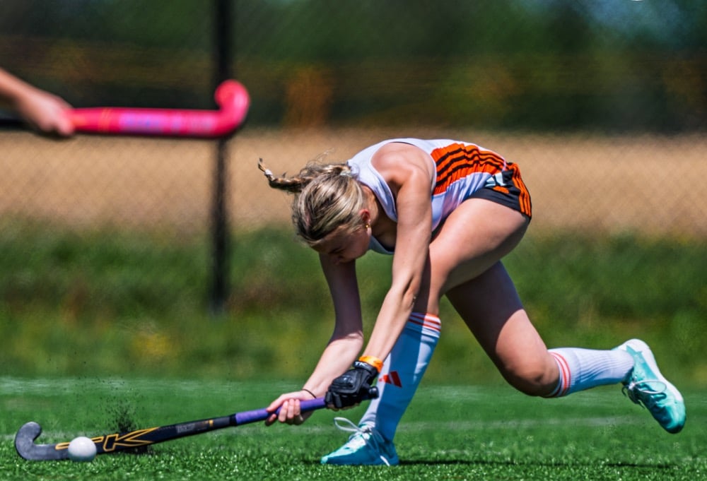 a woman in a white top and orange shorts playing field hockey Madison Falkowski of Surge