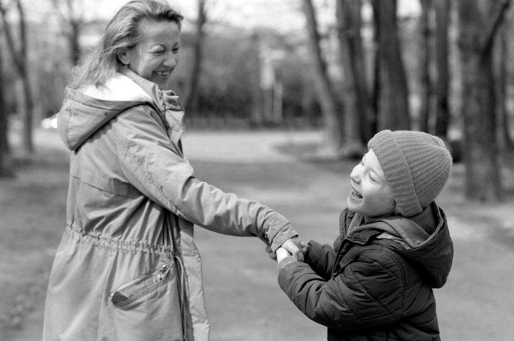 Usmiechnięty chłopiec z wadą wzroku wraz z mamą na ścieżce wśród drzew.