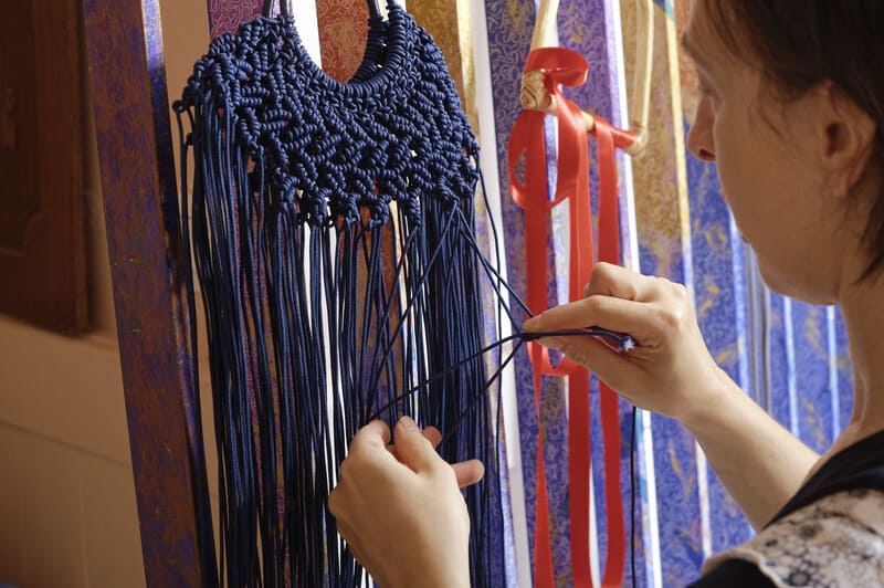 collar azul de macrame con hilos largos colgado en pared