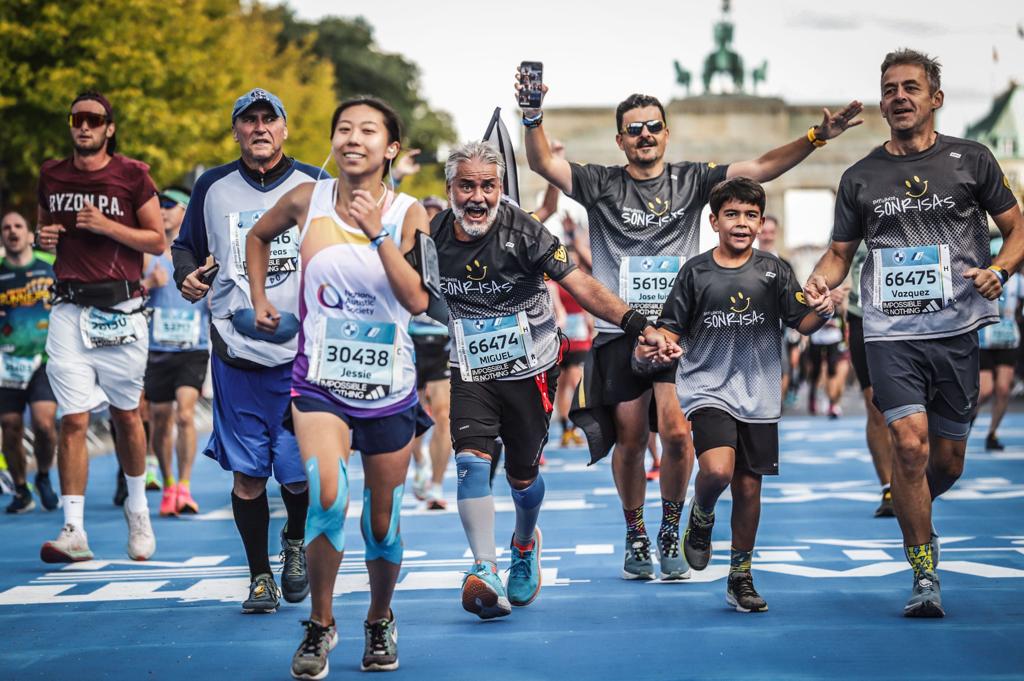 Cuatro corredores de Empujando Sonrisas corren eufóricos con la Puerta de Brandenburgo de fondo