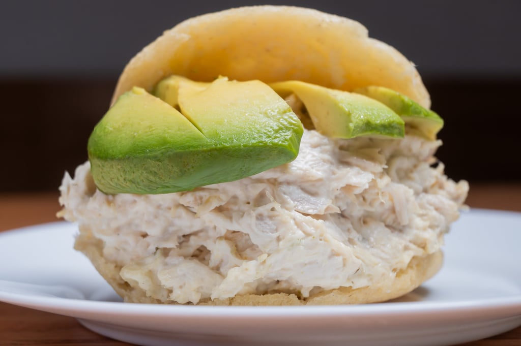 Reina Pepiada arepa stuffed with creamy chicken salad and fresh avocado slices on a white plate.