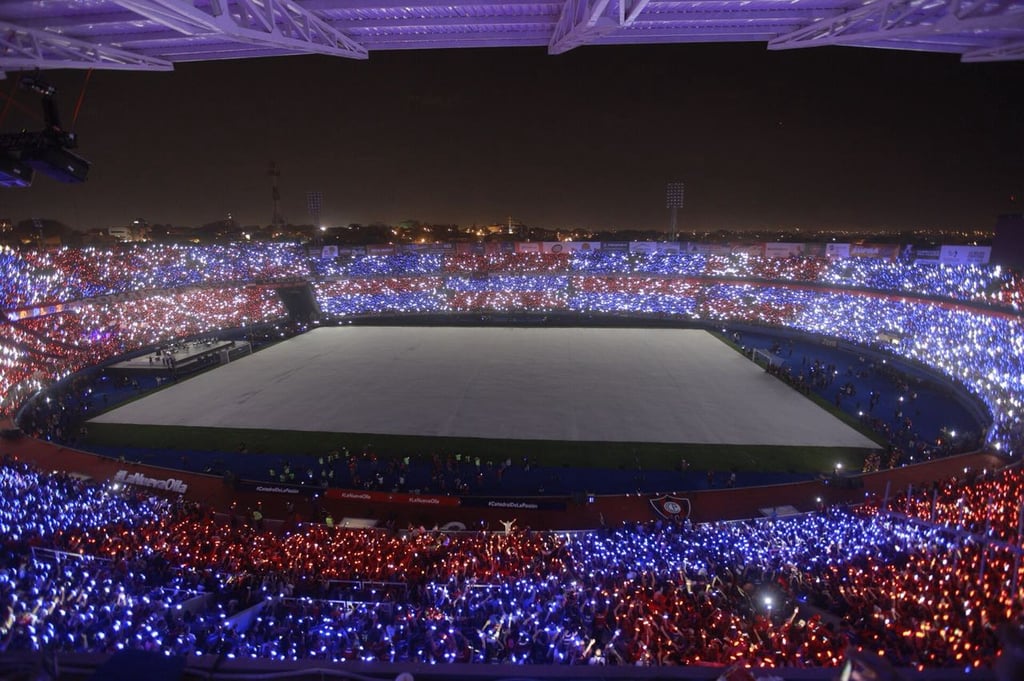 Vista panorâmica das arquibancadas lotadas do estádio La Nueva Olla em Assunção, nas cores azul e vermelho.