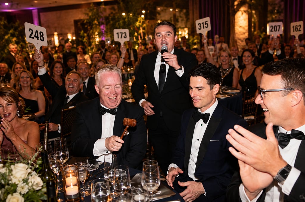 Guests raising bidding paddles during a California fundraising gala while a professional charity auc