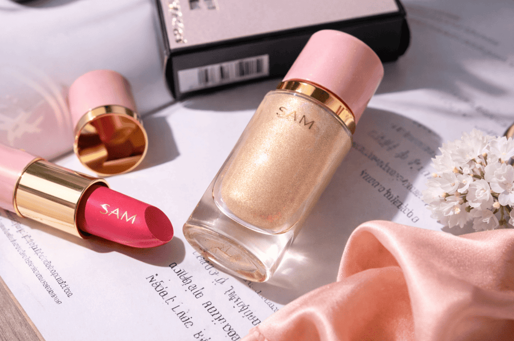 Iluminador líquido dorado de SAM Cosméticos junto a labial sobre fondo elegante.