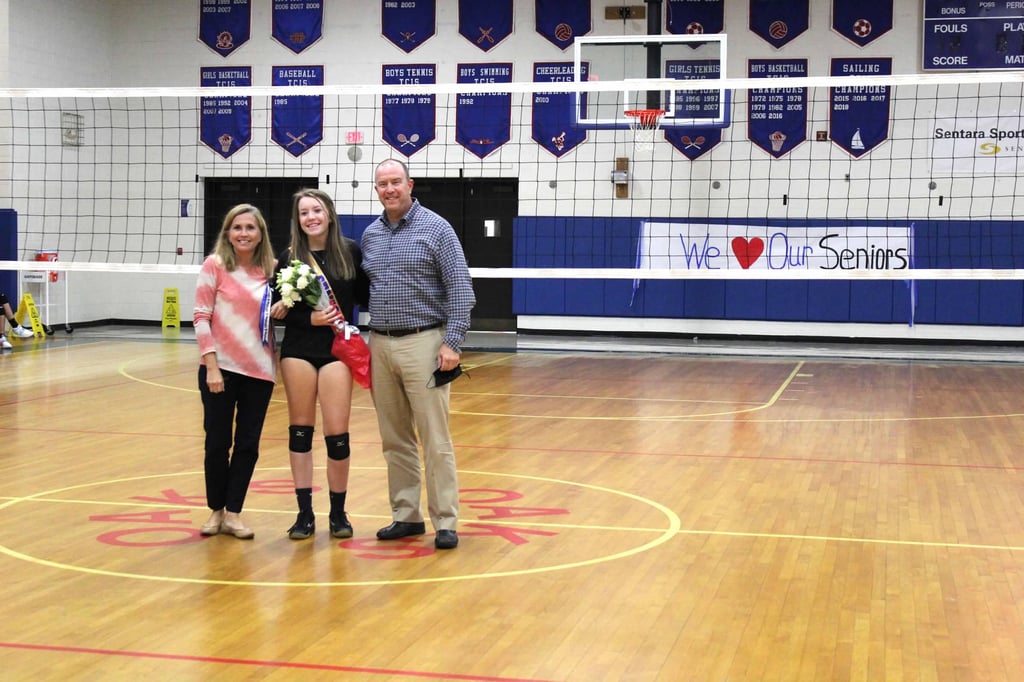 A high school volleyball senior night celebration with a player and her parents on a gym court.