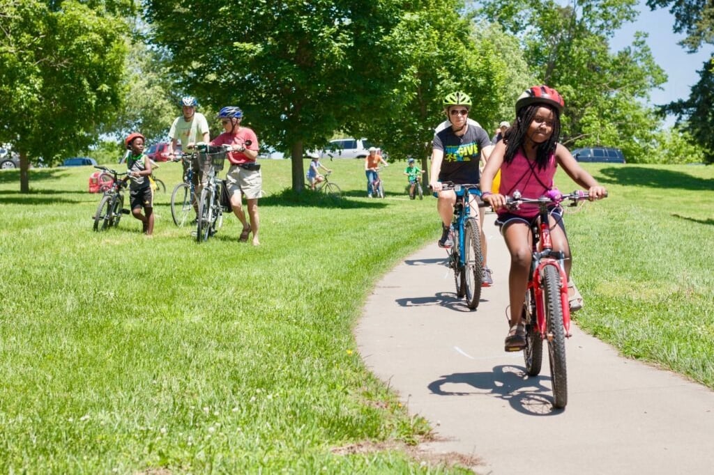 Two people riding bikes on a paved path through a green space
