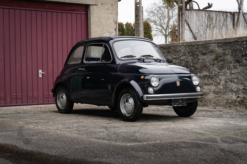 a fiat 500 parked in front of a red garage door