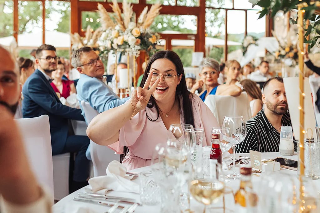 Invitée qui fait un signe de la main drôle alors qu'elle est à table durant un mariage.