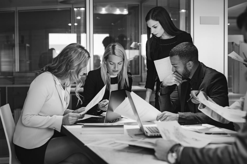 a group of people sitting around a table looking intently at paperwork and screens