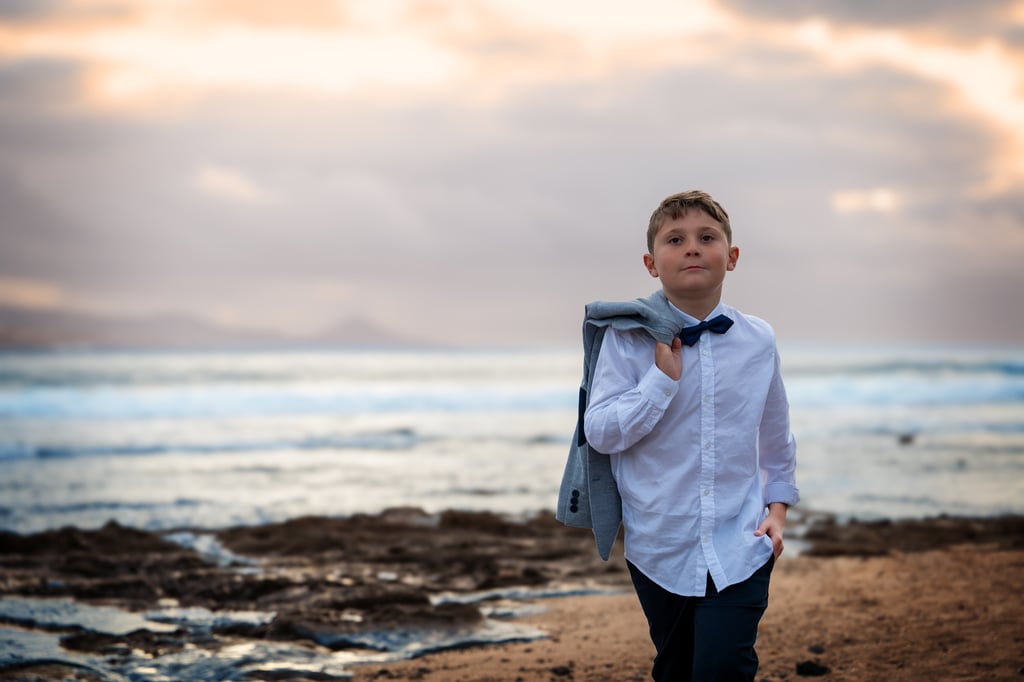 a young boy in a white shirt and tie dye on a beach
