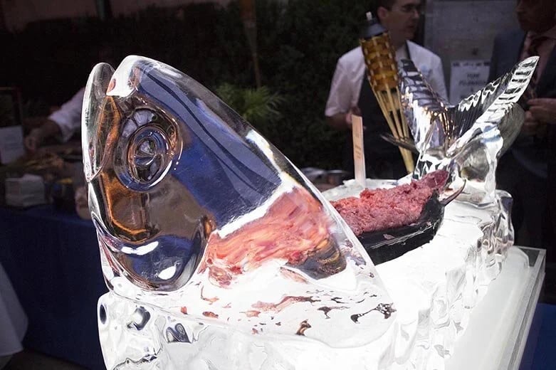 A decorative fish ice sculpture serving fresh tuna tartare at a catered outdoor event.