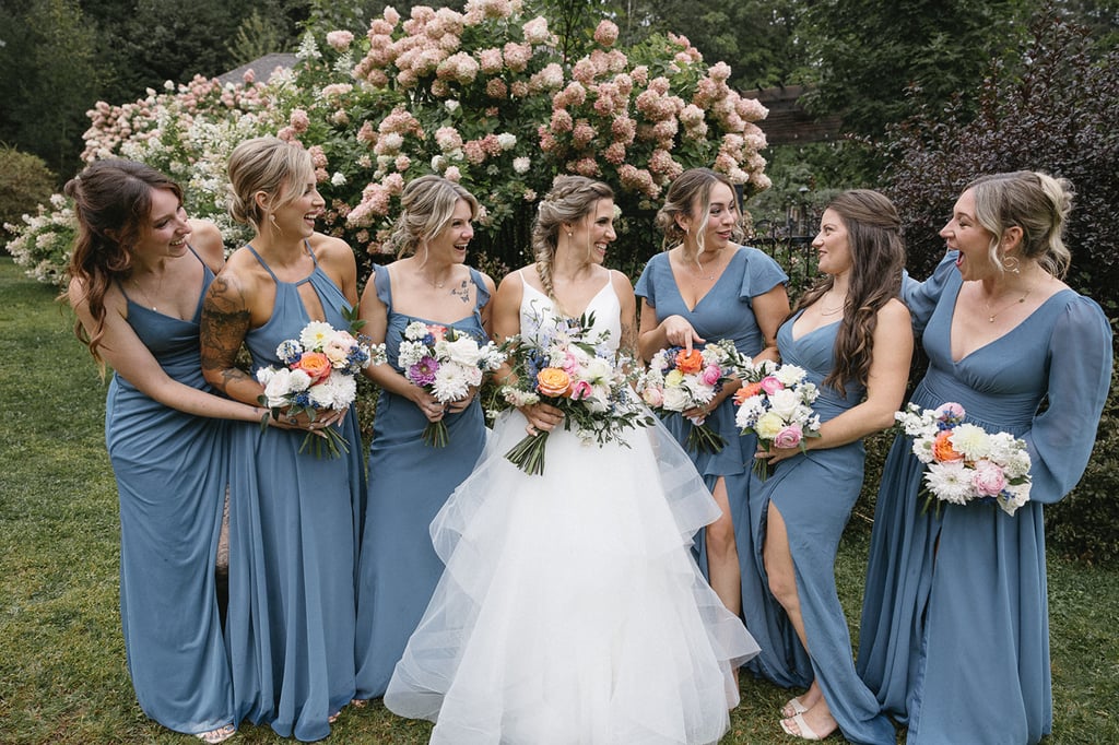 Une mariée et son cortège habillé en bleu se regarde et sourit. Elles tiennent un bouquet de fleurs.