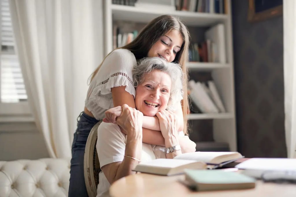 A young woman hugging her happy grandmother at home while reading books together.