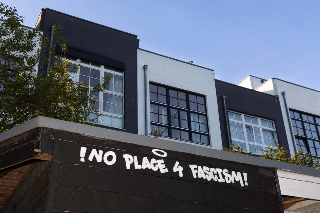 Bild von schwarzen und weißen Häusern, im Vordergrund ist das Graffitti "No room for facism".