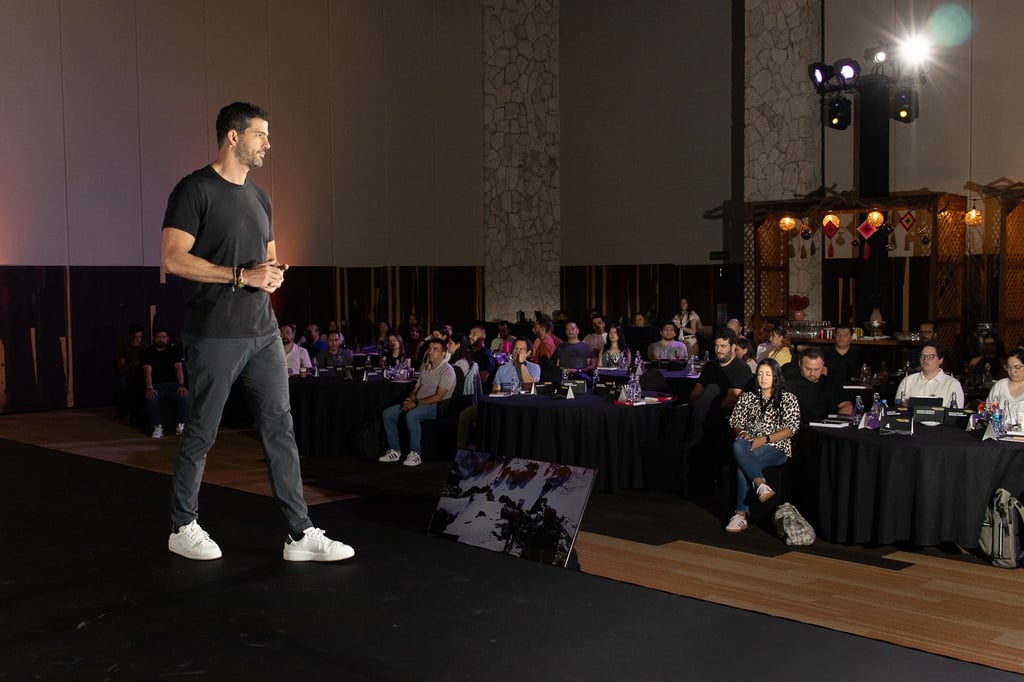 Fotografía de eventos en Cancún. Conferencista Oso Trava exponiendo sobre escenario en salón corporativo.