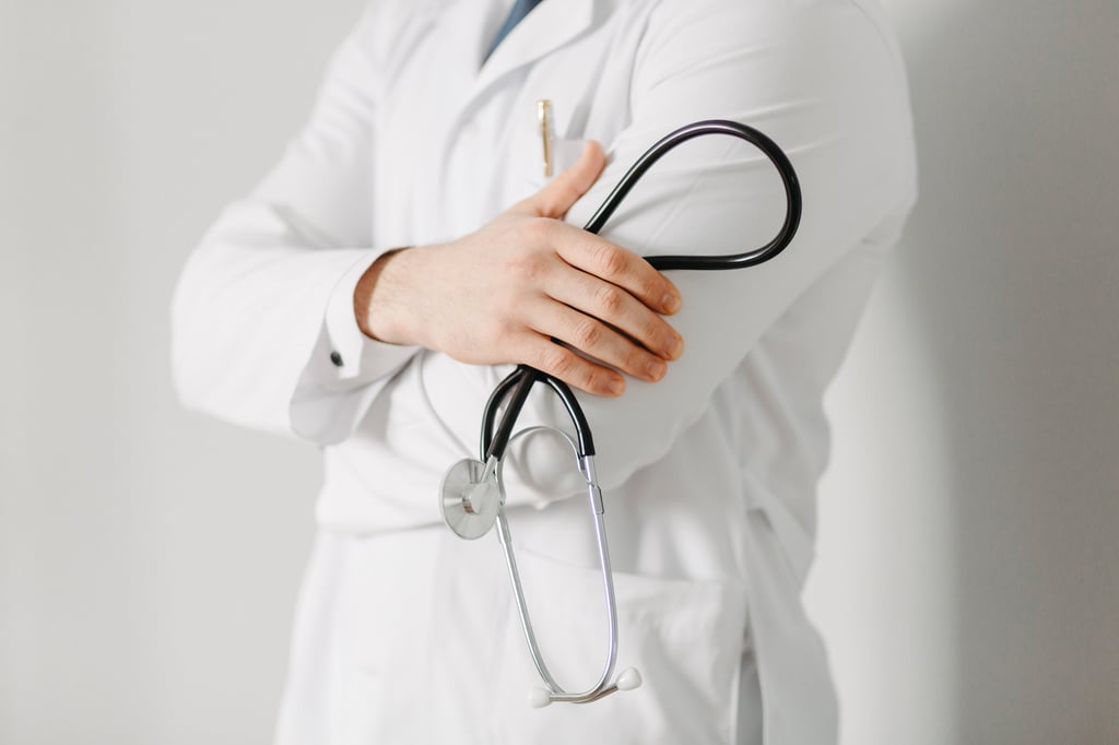 Professional male doctor in white lab coat holding a stethoscope with arms crossed.