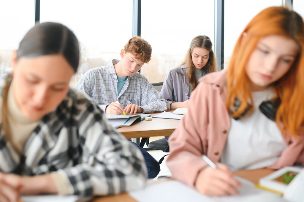 Diverse high school students studying and taking notes in a bright modern classroom.