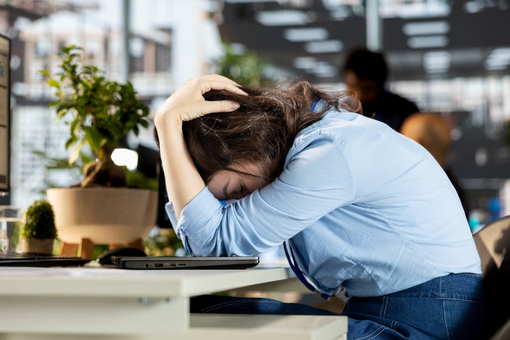 Stressed office worker resting head on desk, illustrating workplace burnout and mental health struggles.