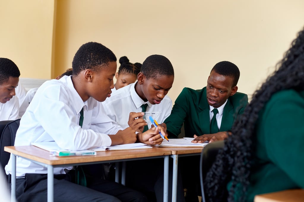 Students in school uniforms collaborating on classwork at a wooden desk in a bright classroom.