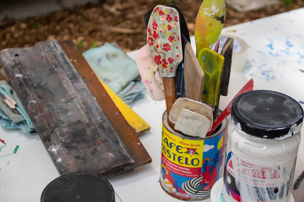 Printmaking materials resting on a table, including spatulas, ink, and a squeegee.