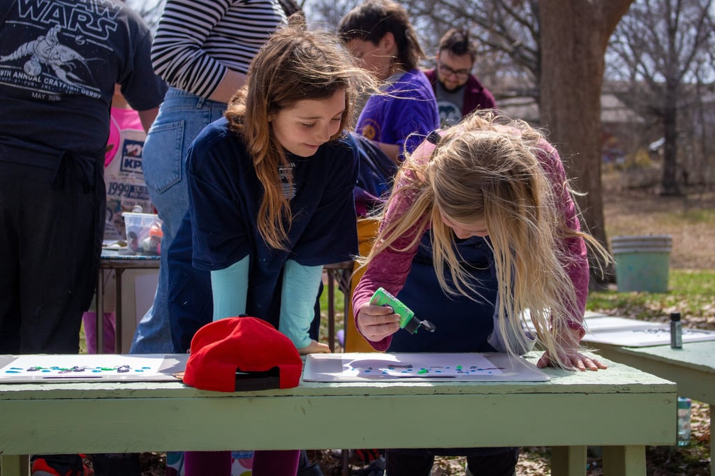 Two young girls smiling while standing over papers dripping paint onto them.