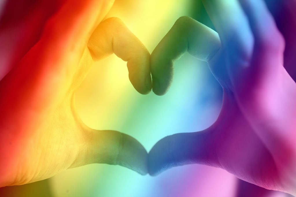 holding hands in a heart shape with a pride rainbow background