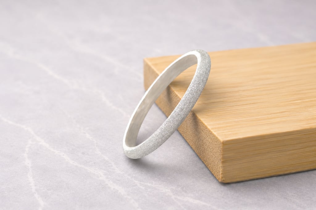 Elegant 999 fine silver ring with a frosted finish resting on a bamboo block over marble background