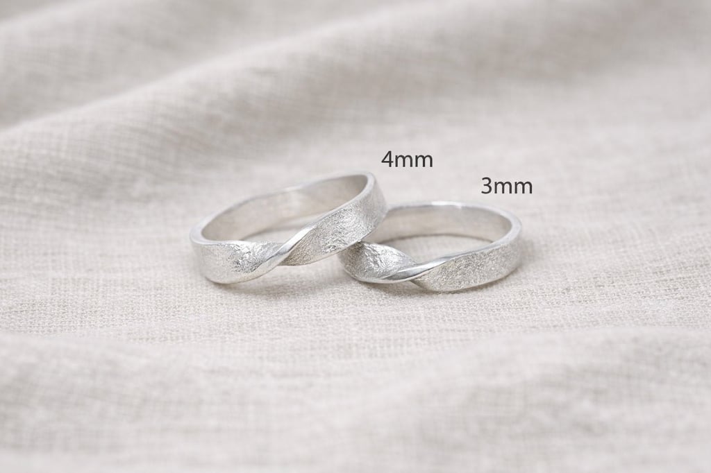 Pair of 999 Fine silver infinity twist wedding bands in 4mm and 3mm widths on linen background.